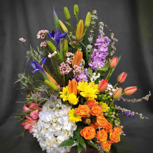 Blue hydrangea, orange lilies, blue irises, orange tulips, yellow daisies, purple stocks, green hypericum, orange spray roses, pink alstroemeria, blue thistle and accented with different fillers and greens all in an 8 x wooden box.